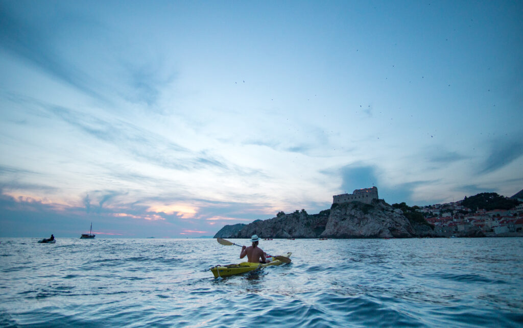 man solo kayaking near the fort and walls of dubrovnik croatia at sunset