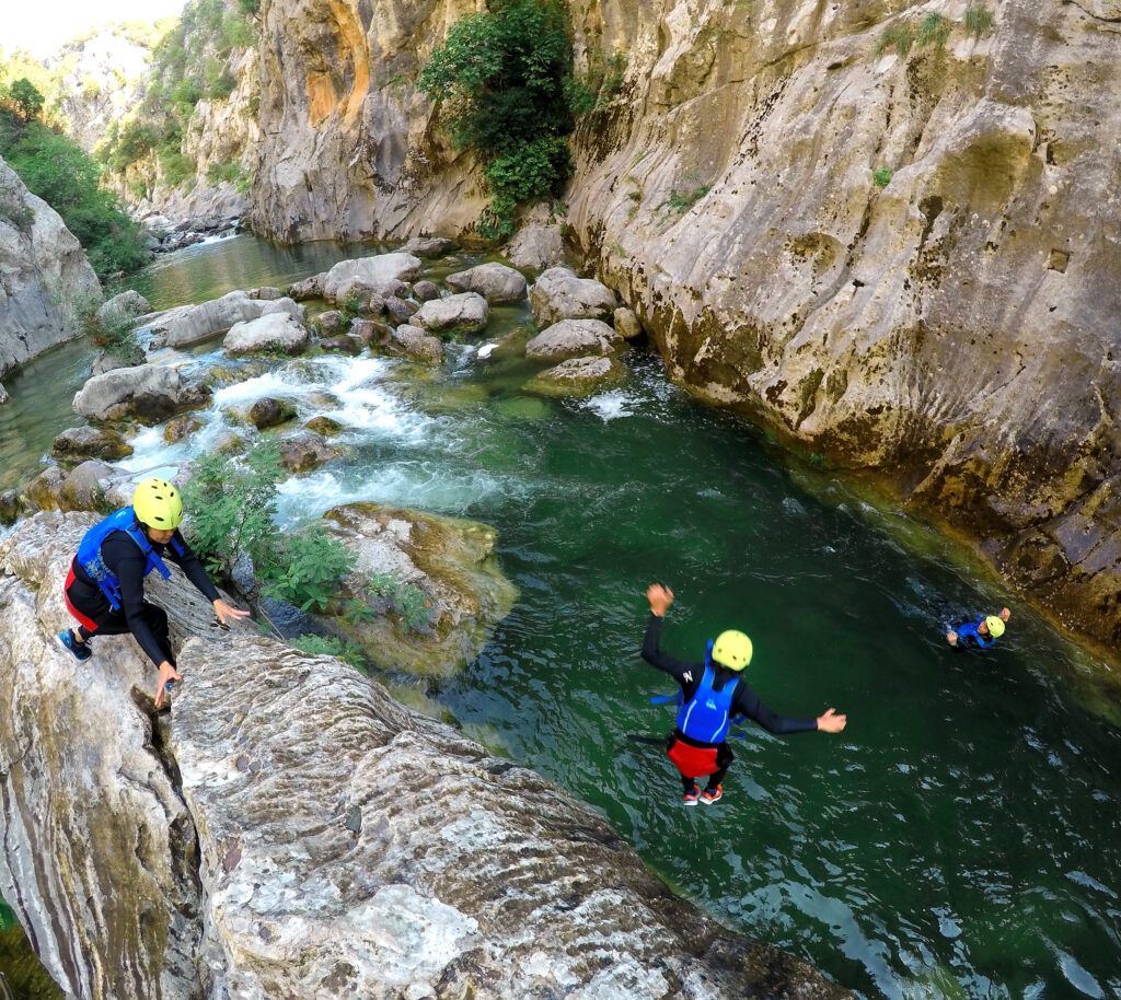 man cliff jumping into a river in croatia blue life vests and yellow helmets