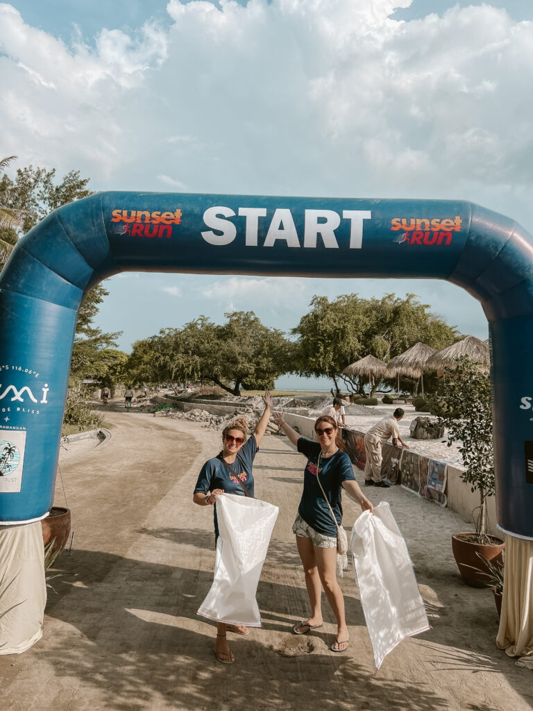 two girls at a beach clean race with white trash bags and blow up race start line